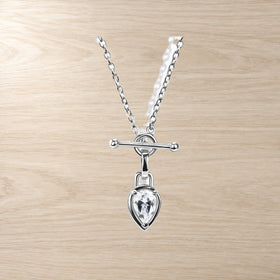 Close-up of a chain necklace with a pear-shaped clear gemstone and horizontal T-bar pendant on wood.