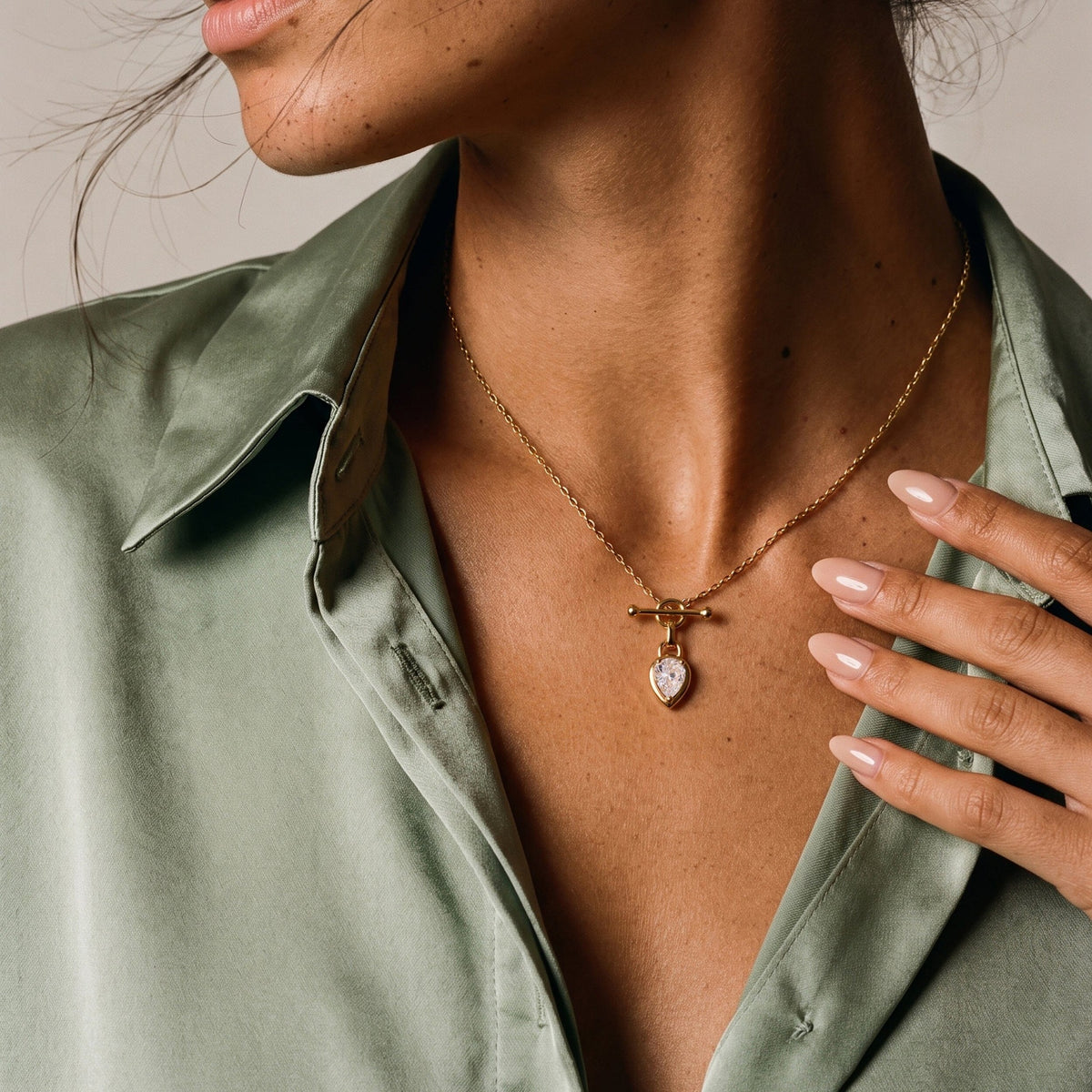 Close view of a pear-shaped faceted pendant worn at the chest, framed by a green shirt and hand.