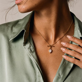 Close view of a pear-shaped faceted pendant worn at the chest, framed by a green shirt and hand.