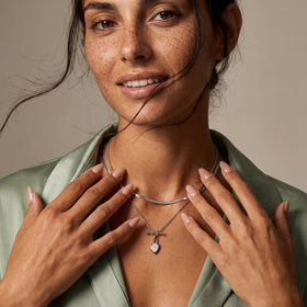 Smiling woman wearing the pear-shaped gemstone necklace, with both hands resting near layered chains.