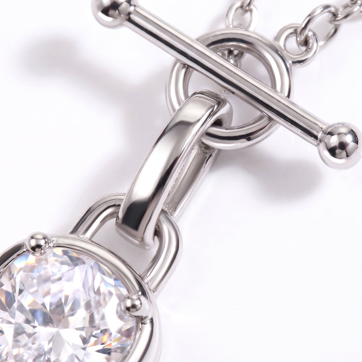 Macro view of a polished T-bar connector, chain links, and faceted clear gemstone setting.