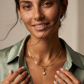 Smiling person models the pear-shaped pendant necklace over layered chains, with hands framing the collar.