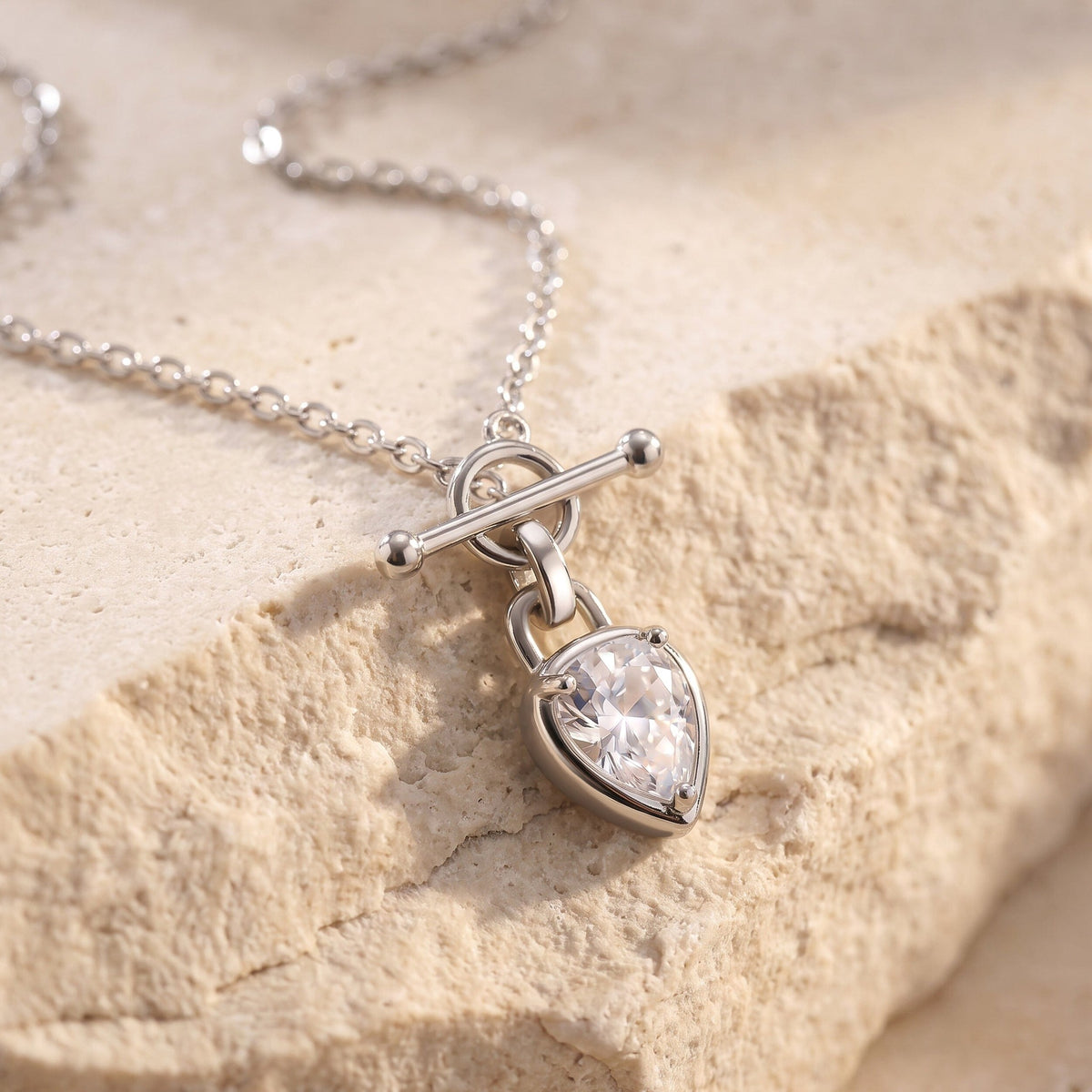 Pear-shaped clear gemstone necklace arranged on a textured stone surface, showing its chain and T-bar closure.