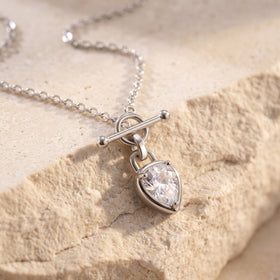 Pear-shaped clear gemstone necklace arranged on a textured stone surface, showing its chain and T-bar closure.