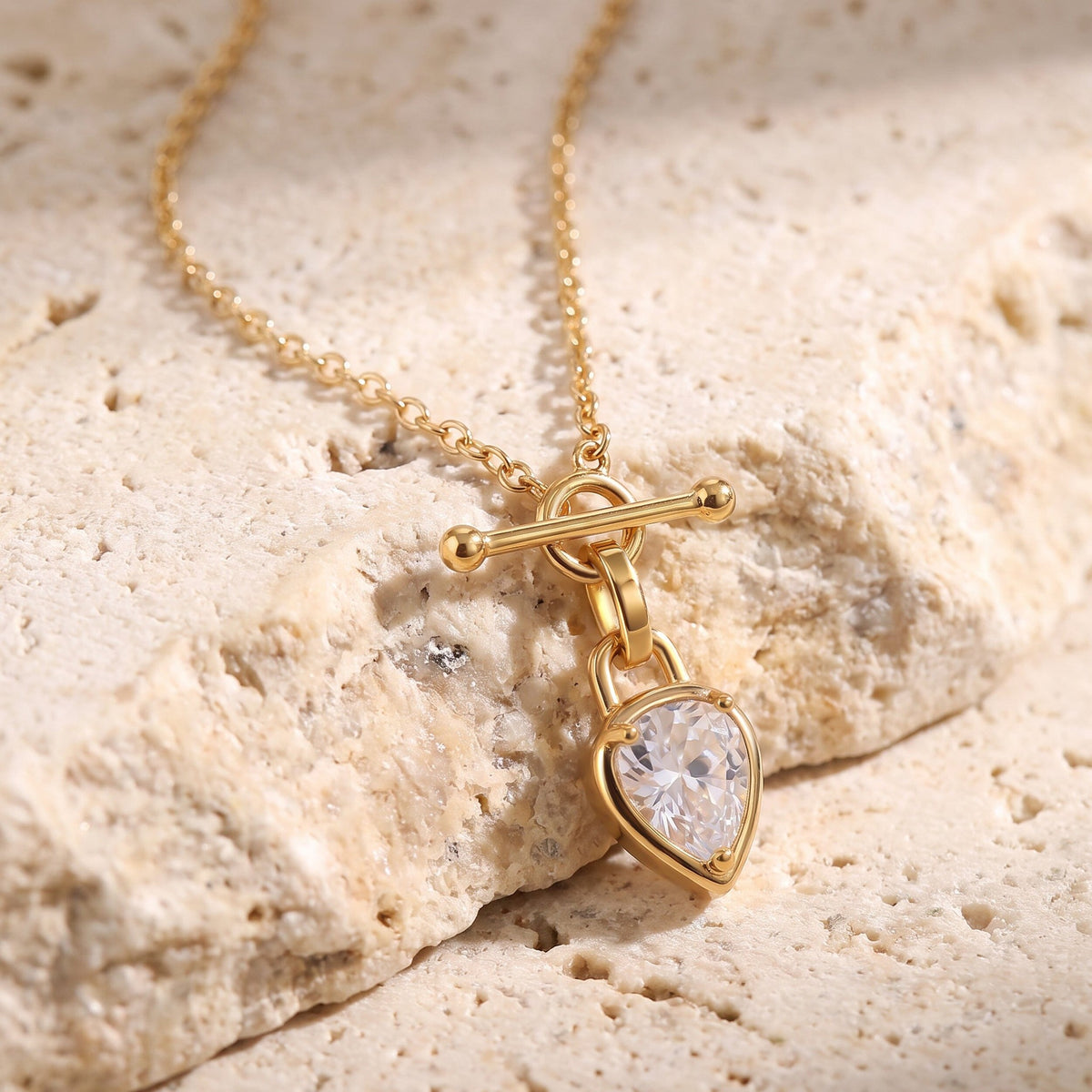 Pendant necklace displayed on rough stone, featuring a pear-shaped faceted clear gem and linked chain.