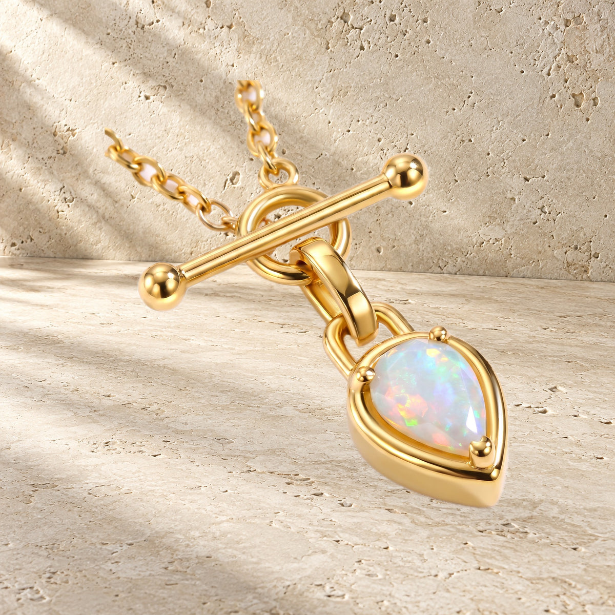 Close-up of the necklace's T-bar and pear-shaped iridescent gemstone resting on a textured surface.