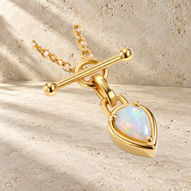 Close-up of the necklace's T-bar and pear-shaped iridescent gemstone resting on a textured surface.