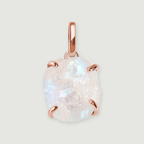 A raw moonstone pendant with four rose gold prongs and an elongated bail rests on a light gray background.