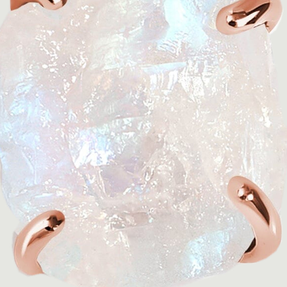 Blue and pearly flashes appear across the uneven surface of the moonstone between rose gold prongs.