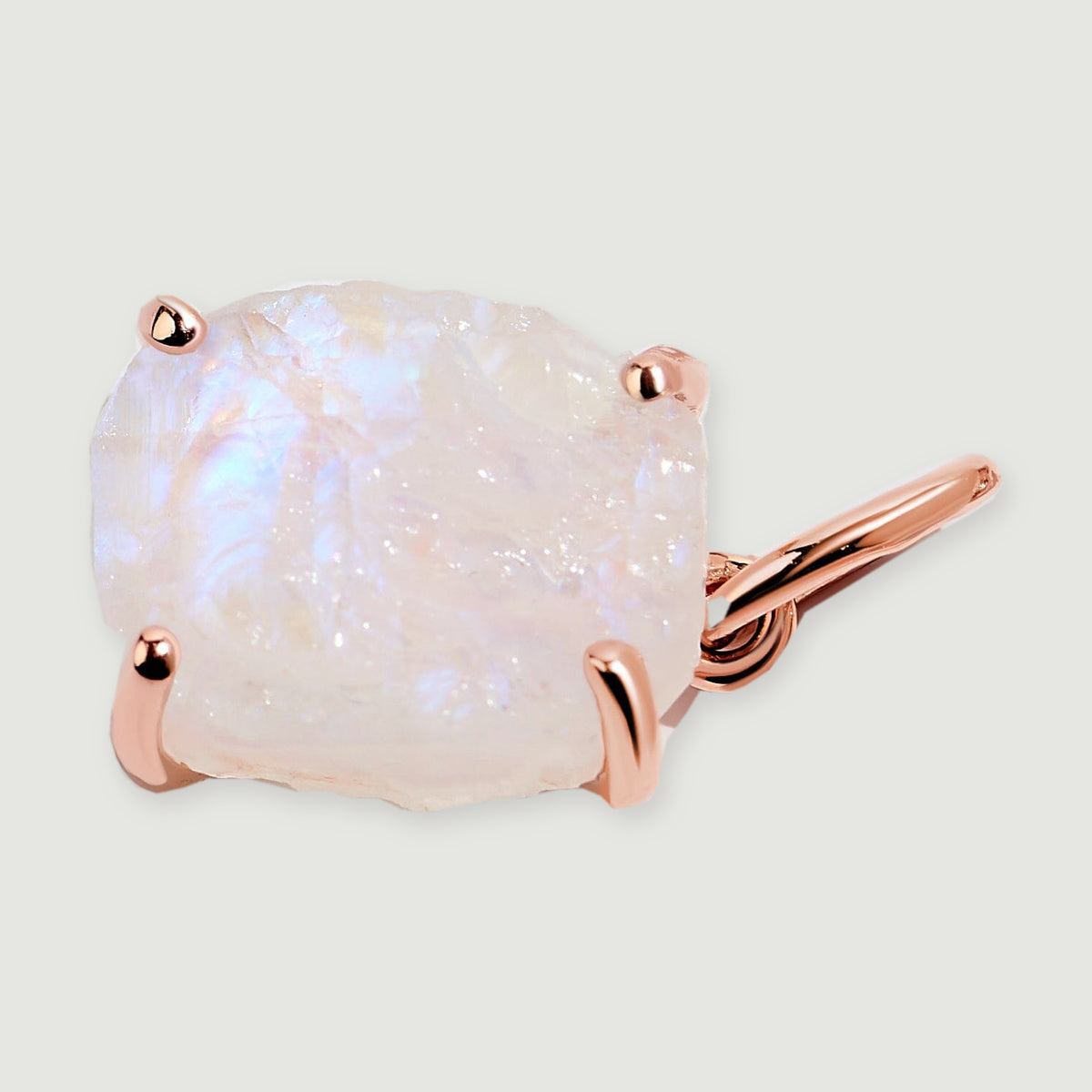 The moonstone charm lies on a pale gray surface with its rose gold bail extending to the right.