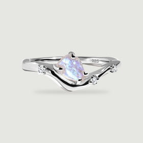 A sterling silver wishbone ring holds a rough moonstone and three small clear stones on a light gray surface.