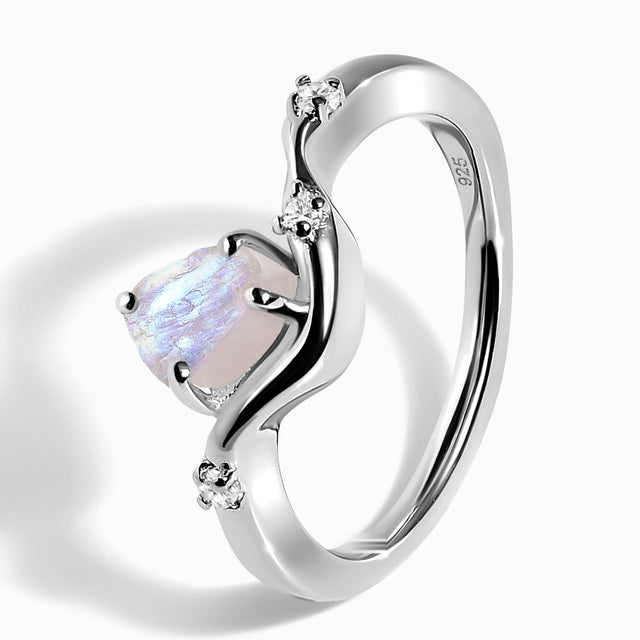 The sterling silver ring rests at an angle on a light tabletop, showing its raised moonstone, curved band, and 925 stamp.