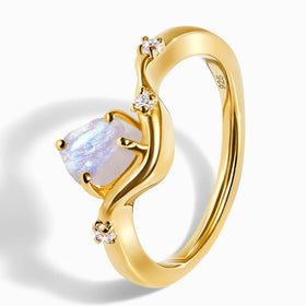 The yellow gold vermeil ring lies at an angle, with its rough moonstone, clear accent stones, and open band visible.