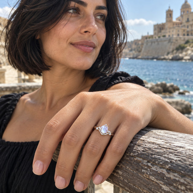 A woman wears the silver moonstone ring while resting her hand on a wooden railing beside blue water.