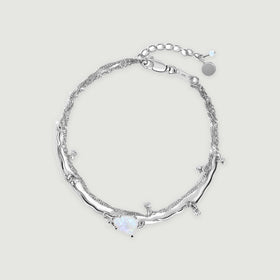 A sterling silver bracelet forms an oval with an irregular pale moonstone, a double chain and a lobster clasp on a light gray surface.