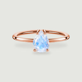 A pear-shaped moonstone sits in four rose gold prongs above a polished ring band on a light gray background.