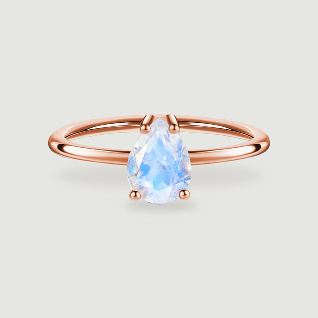 A pear-shaped moonstone sits in four rose gold prongs above a polished ring band on a light gray background.