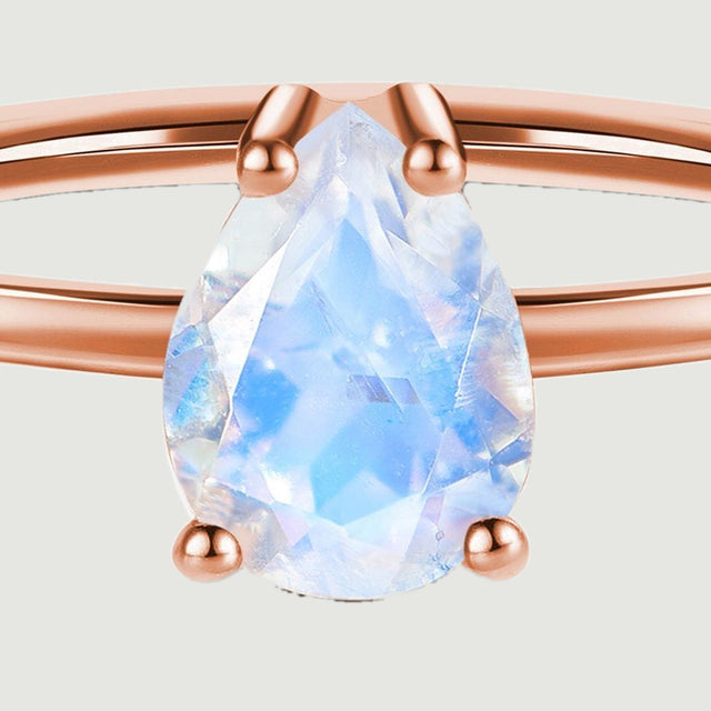 The close-up reveals pale blue facets inside the pear-shaped moonstone and its four rounded prongs.