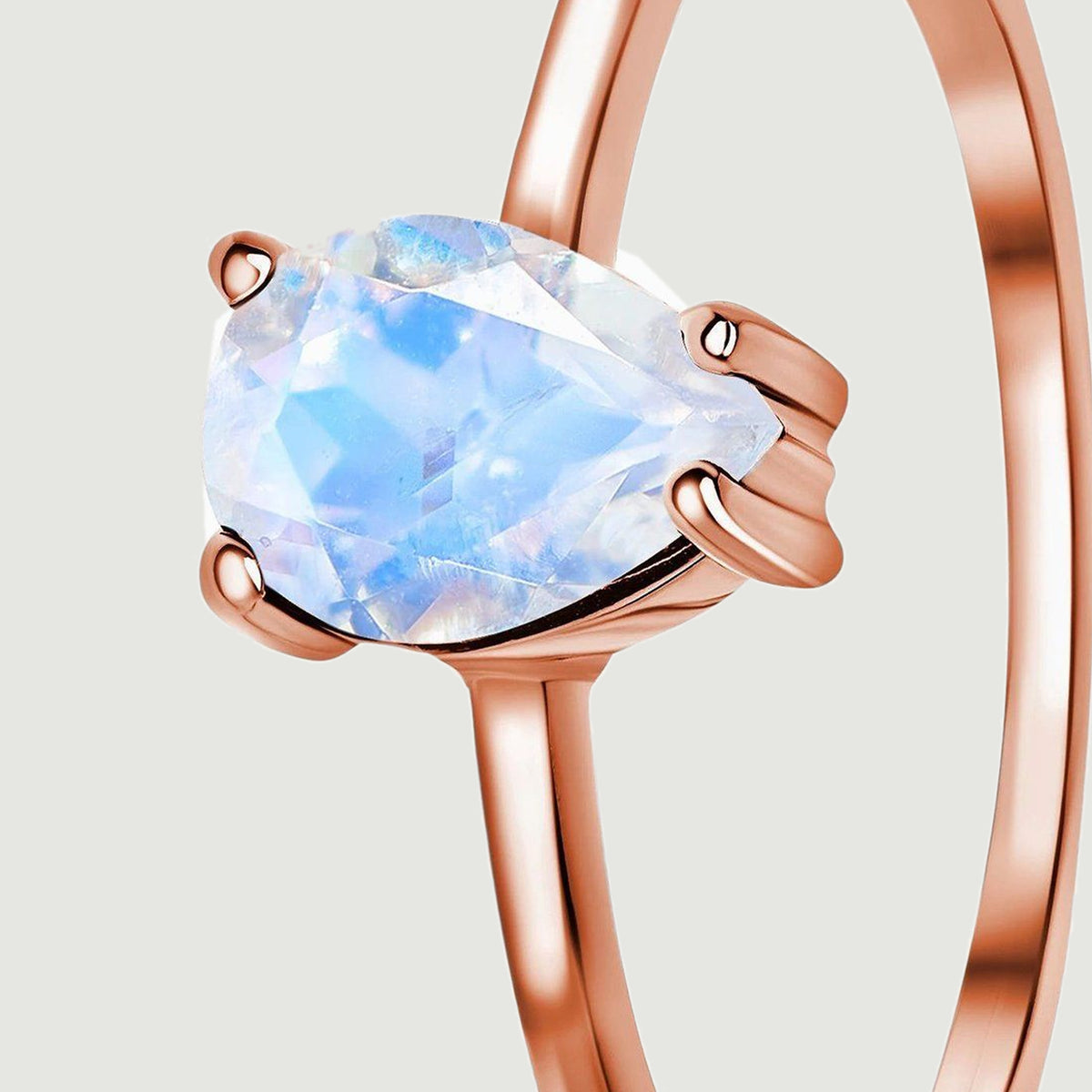 A three-quarter close-up shows the rounded rose gold prongs and the slender band beside the pear-shaped moonstone.