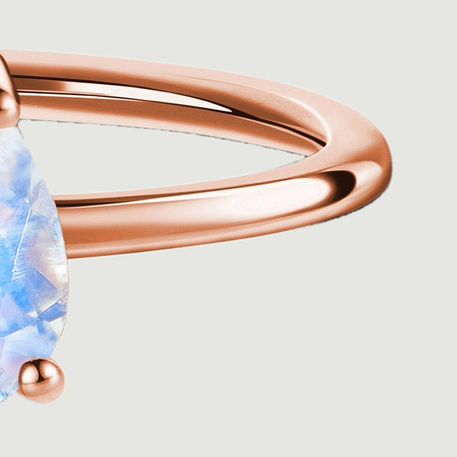 The polished right shoulder of the rose gold ring curves beside the lower moonstone prong.