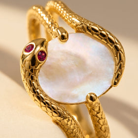 A close view shows the white oval center, two red stones, and polished yellow gold textured edges.