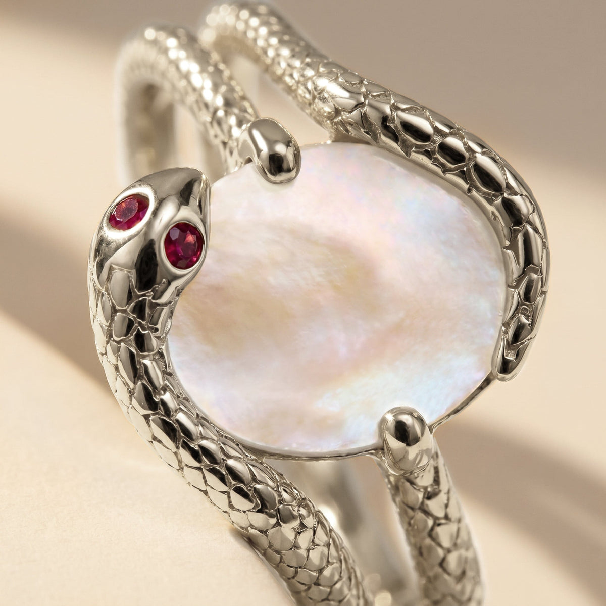 Two red stones and silver textured curves border an iridescent white oval in this close view.