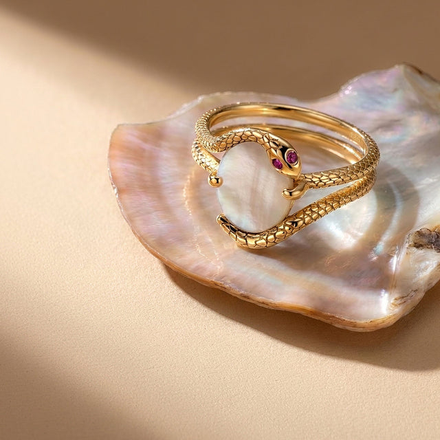 The yellow gold wrap ring rests on an open pearlescent shell over a warm neutral tabletop.