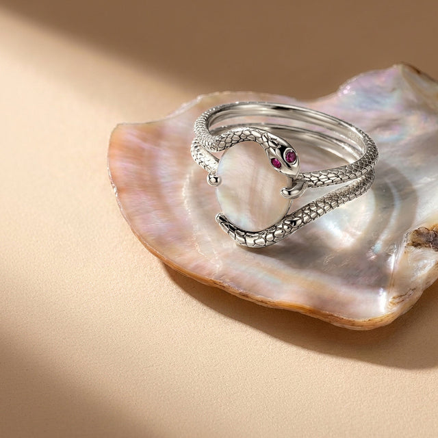 The silver ring is angled on a pearlescent shell with its wrapped bands and white center visible.