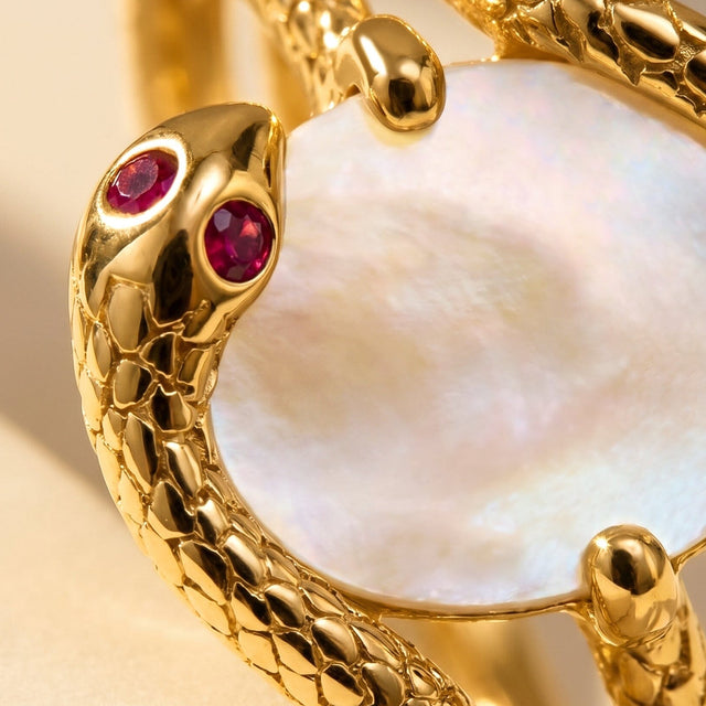 A tight crop reveals red faceted accents beside the pearly center and the textured yellow gold band.